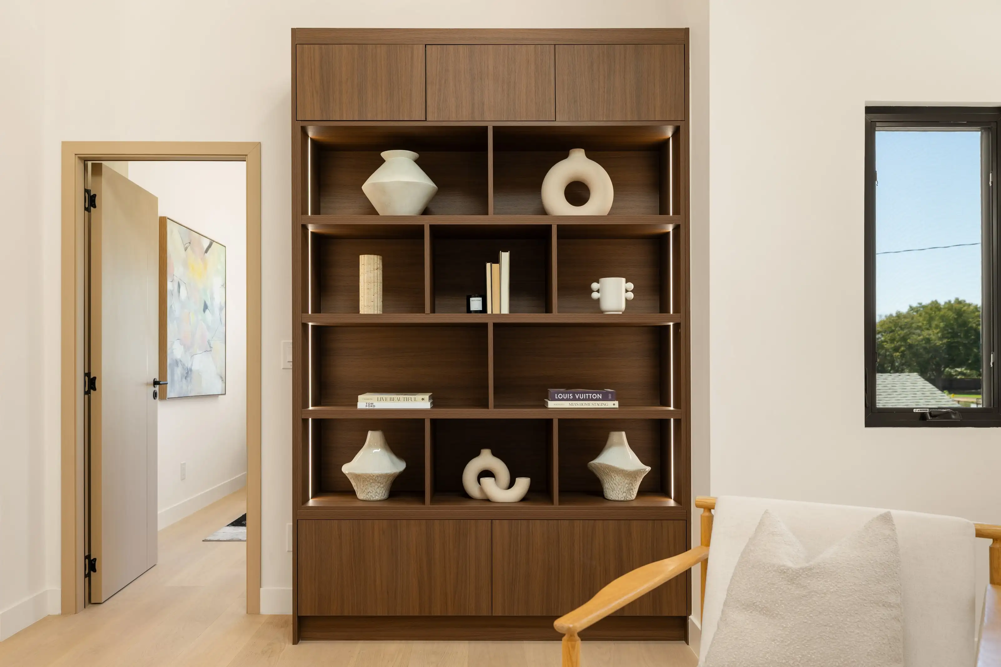 Walnut built-in display shelving with integrated LED lighting, flat panel doors above and below, styled with ceramics and books
