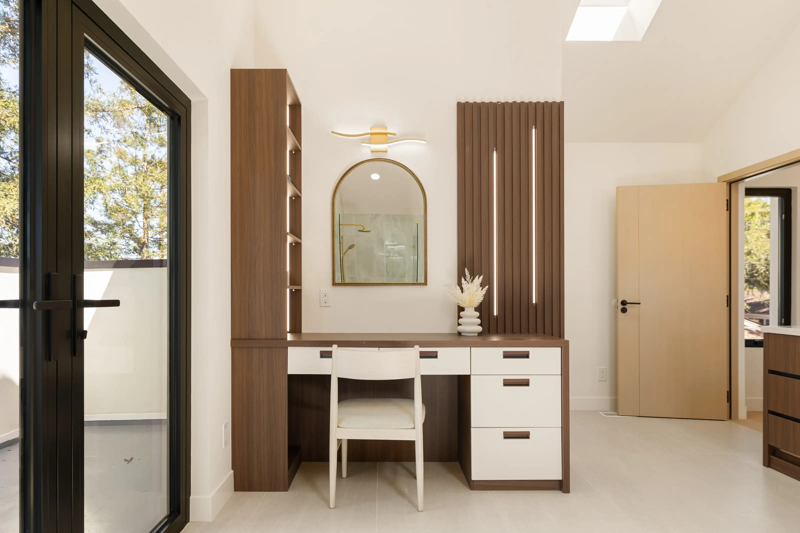 Built-in walnut and white vanity desk with arched brass mirror, fluted walnut slat panel and integrated vertical lighting