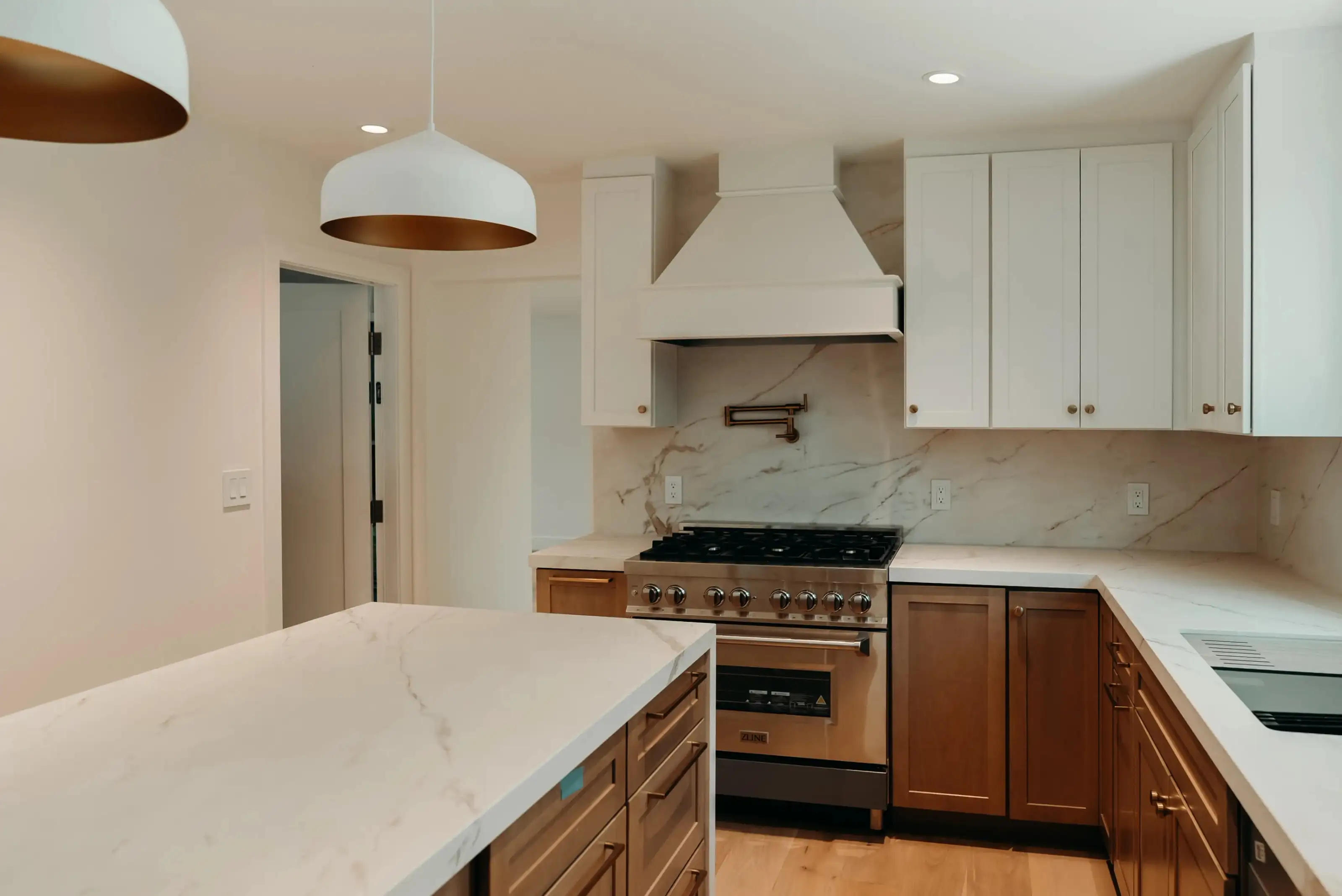 Kitchen remodeling project with ZLINE range, white custom hood, marble backsplash, quartz island, and warm wood cabinets