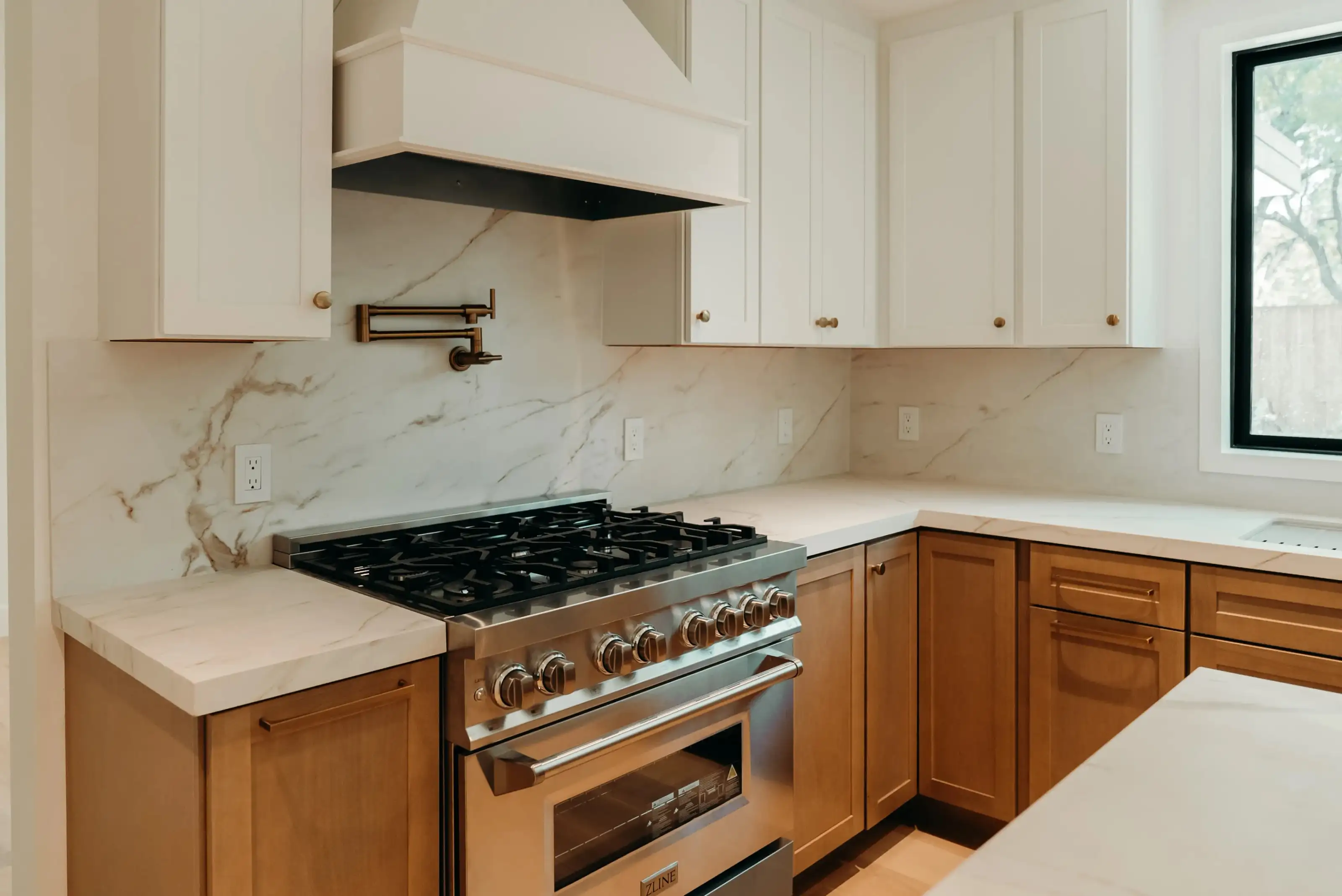 Stainless steel ZLINE 6-burner gas range with custom range hood, marble backsplash, and warm wood lower cabinets in a