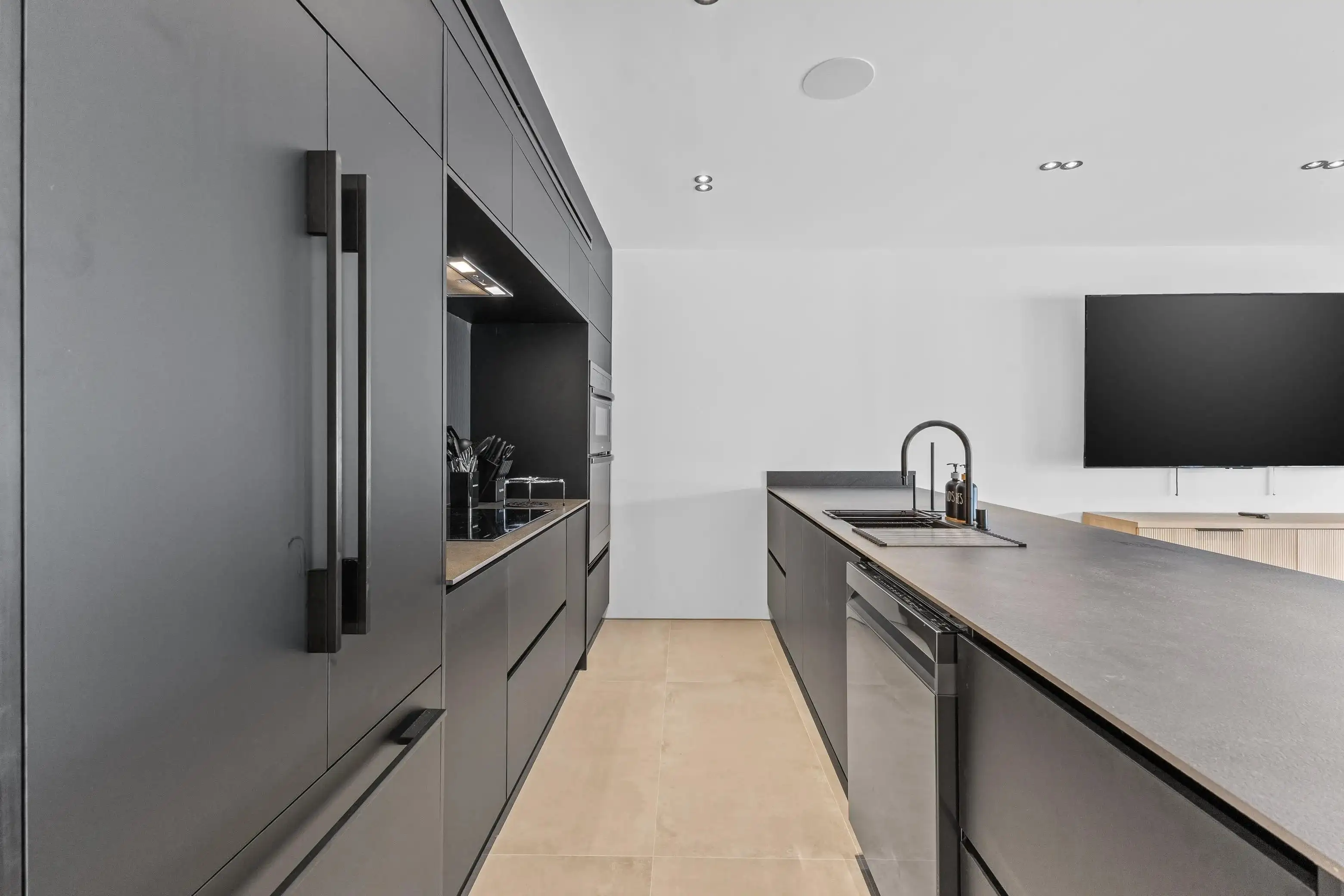 Modern kitchen remodel with dark gray flat-panel cabinets, stone countertops, black faucet, and light tile flooring