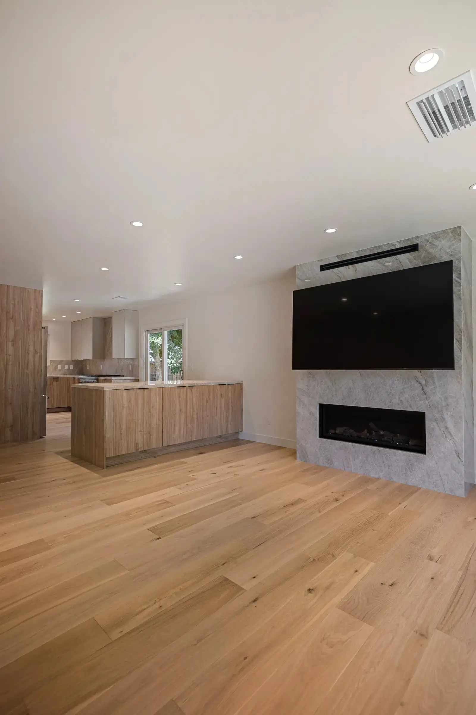 Open-concept kitchen remodel with wood island, marble fireplace wall, wall-mounted TV, and light hardwood floors