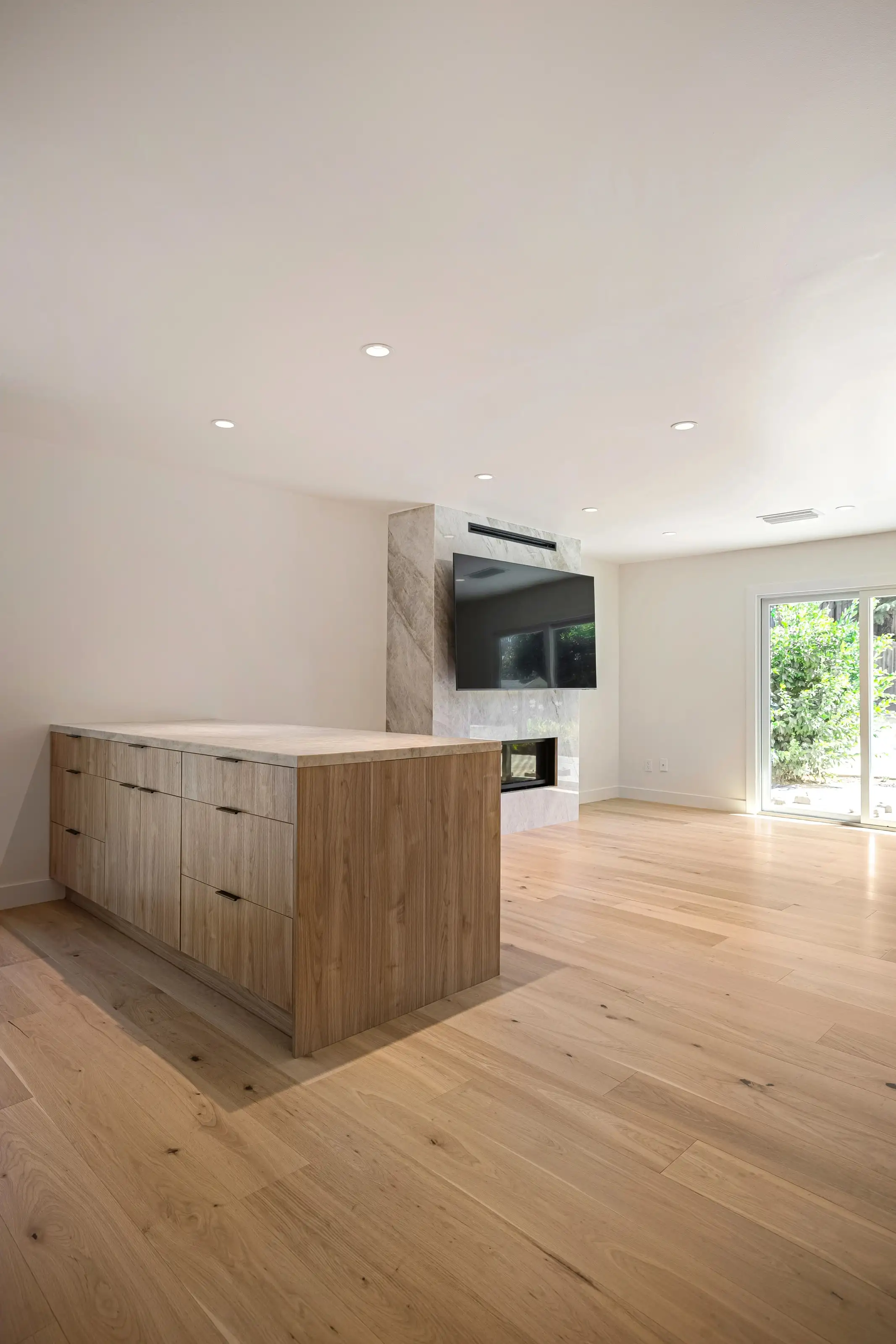 Modern living area renovation in San Jose featuring marble accent wall with mounted TV, wood cabinetry, and light hardwood flooring.