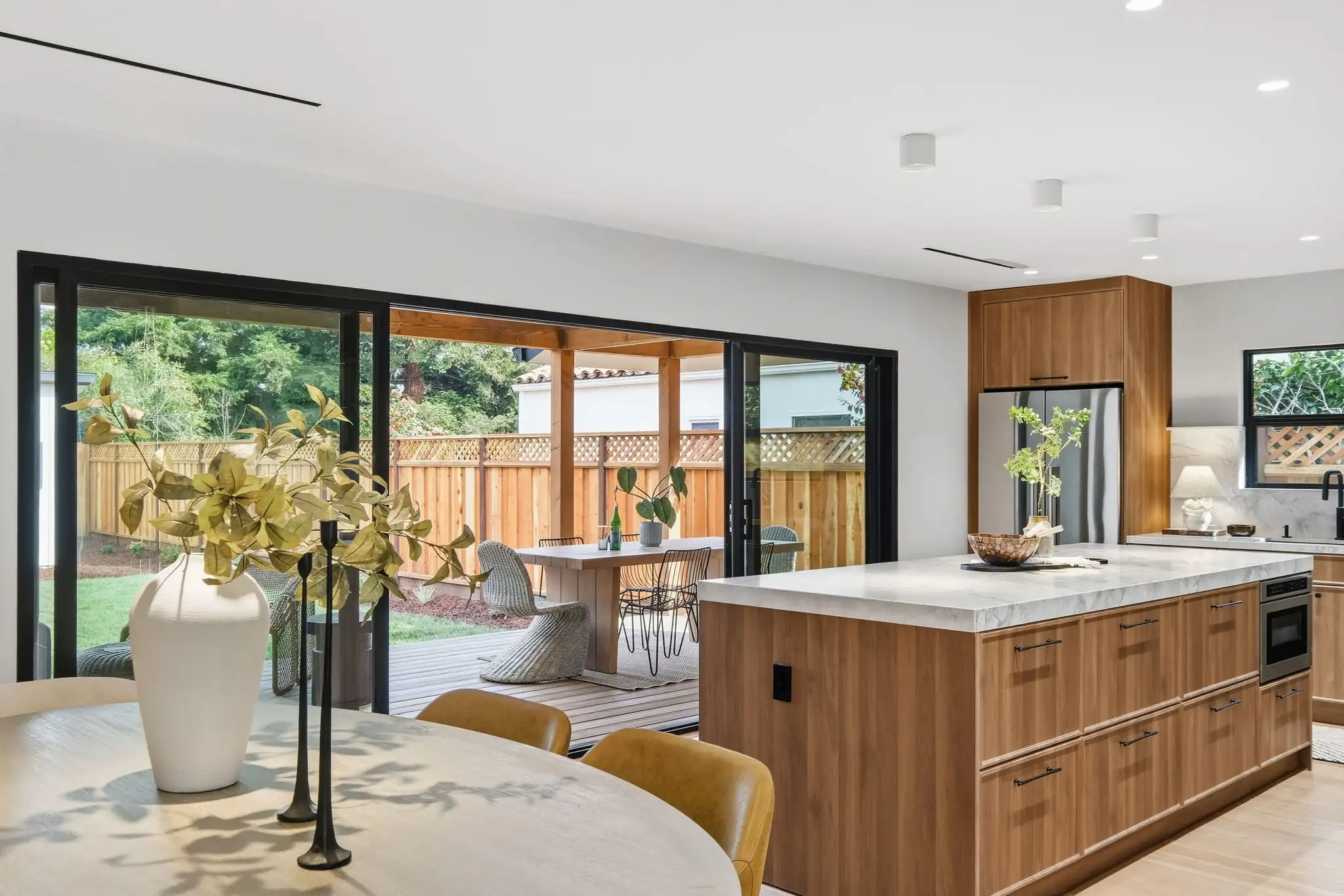 Open-concept kitchen remodel with wood cabinetry, marble island, and folding glass doors opening to a backyard deck patio.