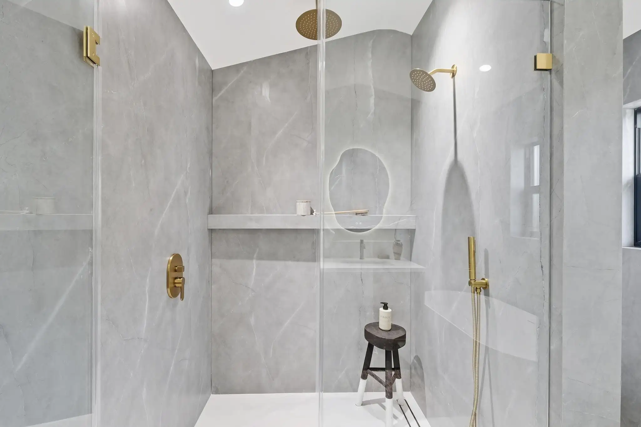 Luxury bathroom remodeling with gray marble walls, gold rain shower fixtures, glass partition, and built-in shelf niche