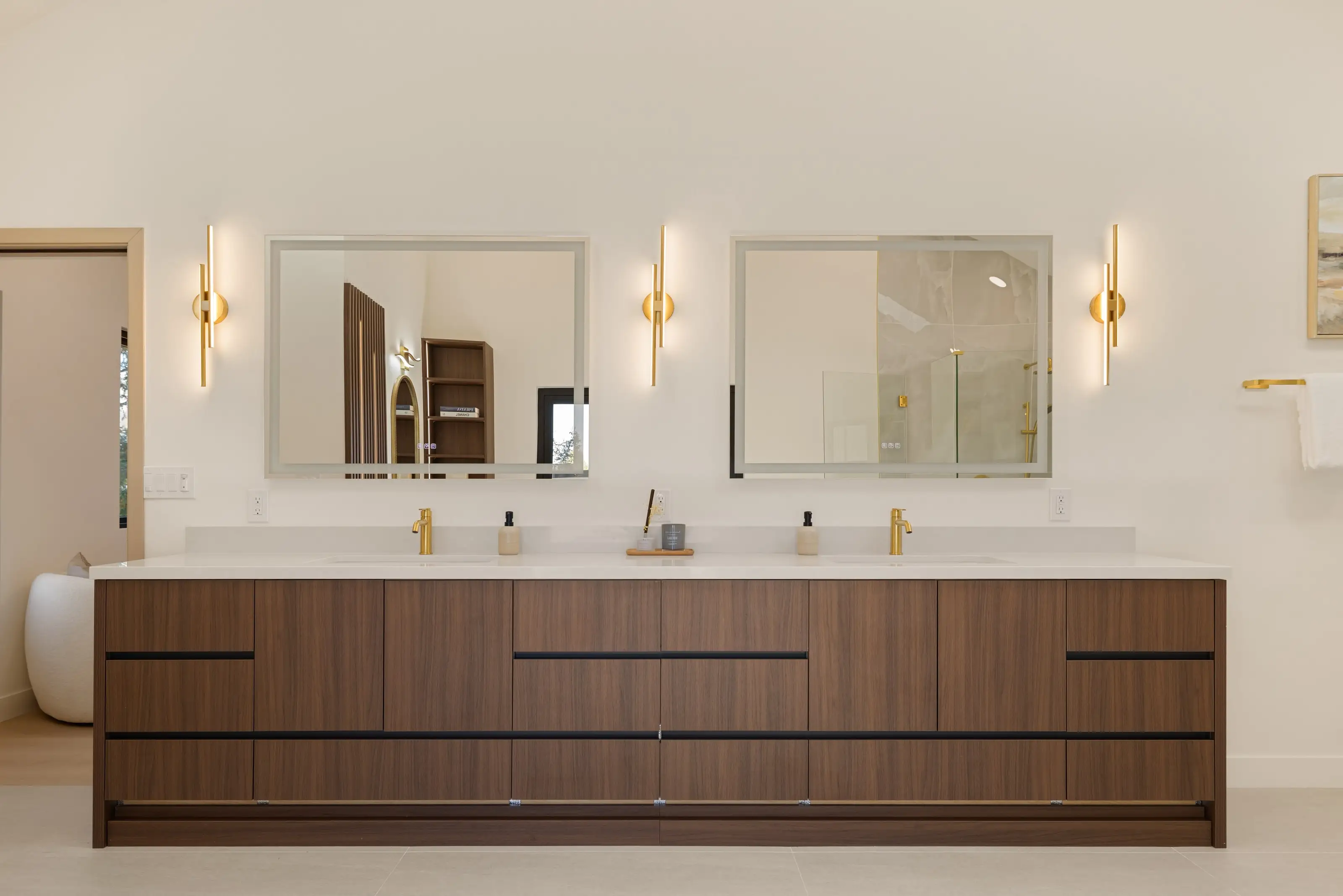 Walnut double vanity with a white quartz top, brass faucets, paired mirrors and three linear brass sconces